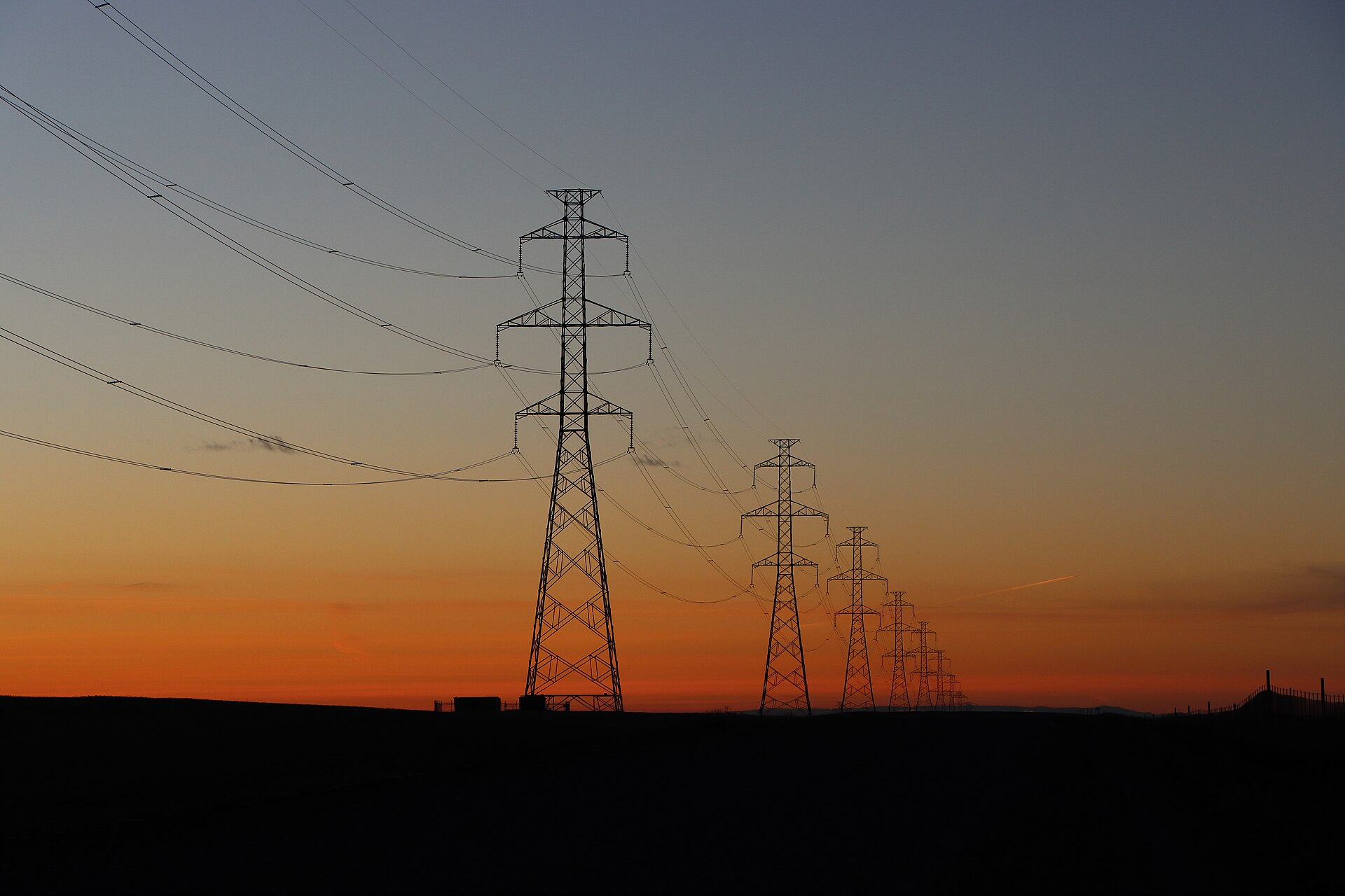 A line of high-voltage transmission towers carrying power across the grid at sunset