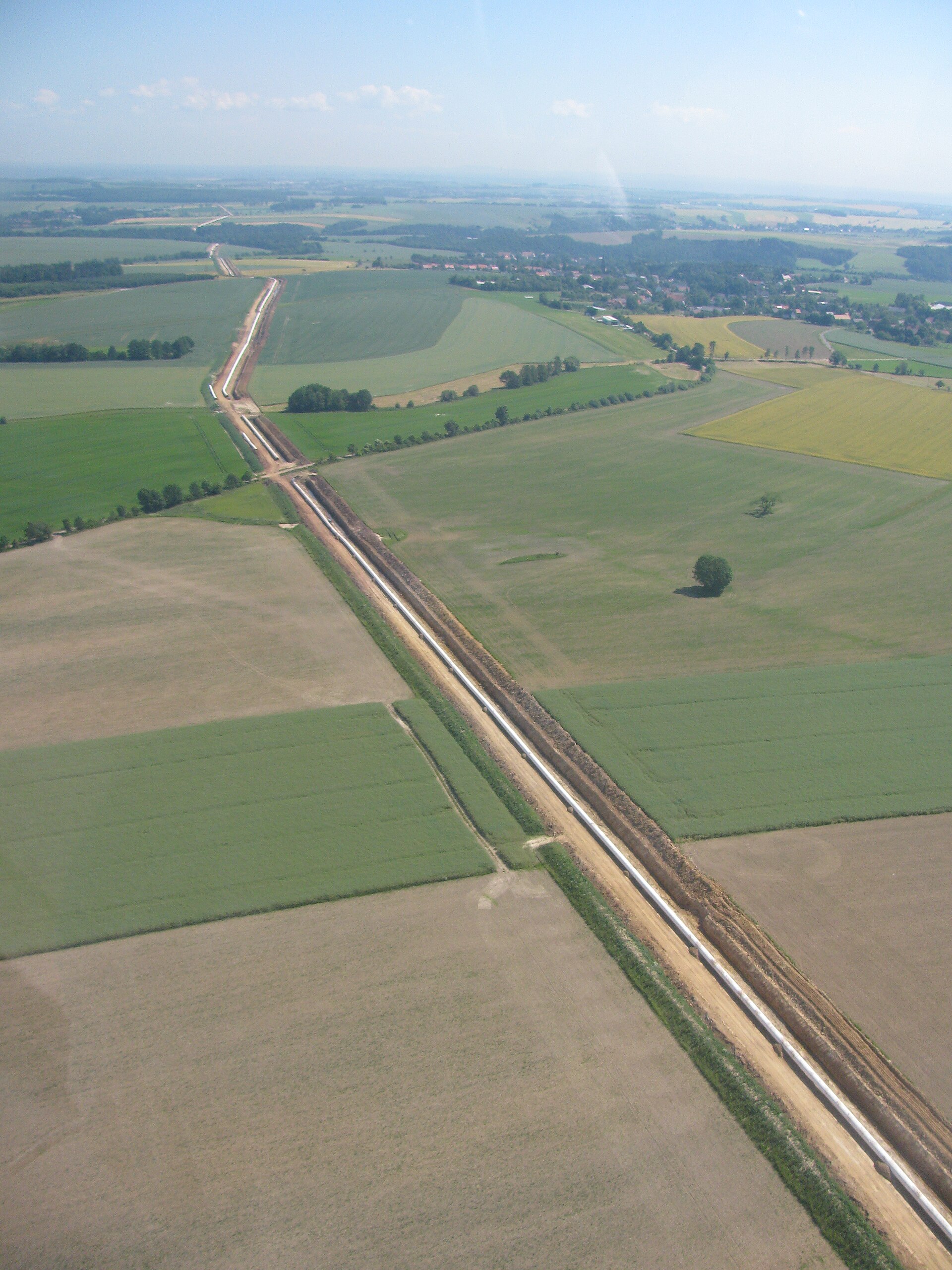 Aerial view of a long straight gas pipeline trench crossing farmland