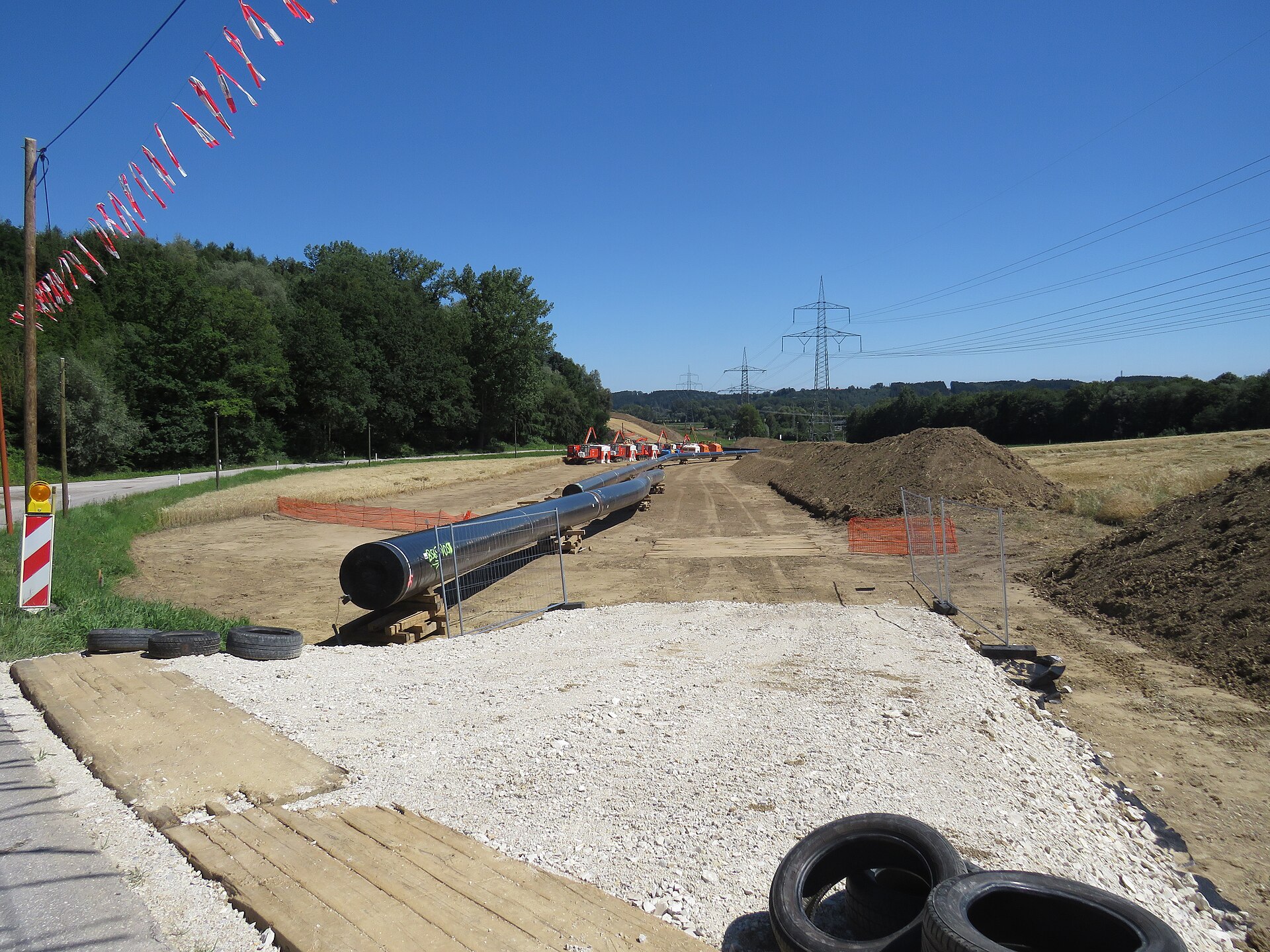 Coated steel pipe sections laid out beside a fenced trench during gas pipeline construction